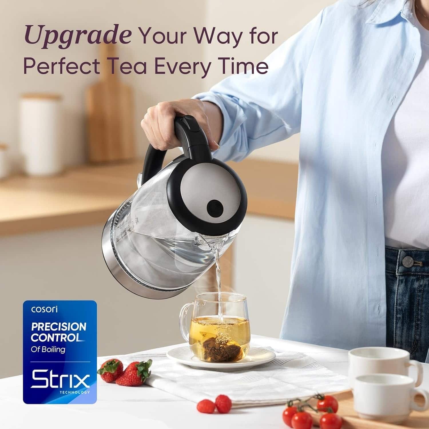 Stainless steel electric kettle pouring hot water for tea on a kitchen counter with strawberries and cups.